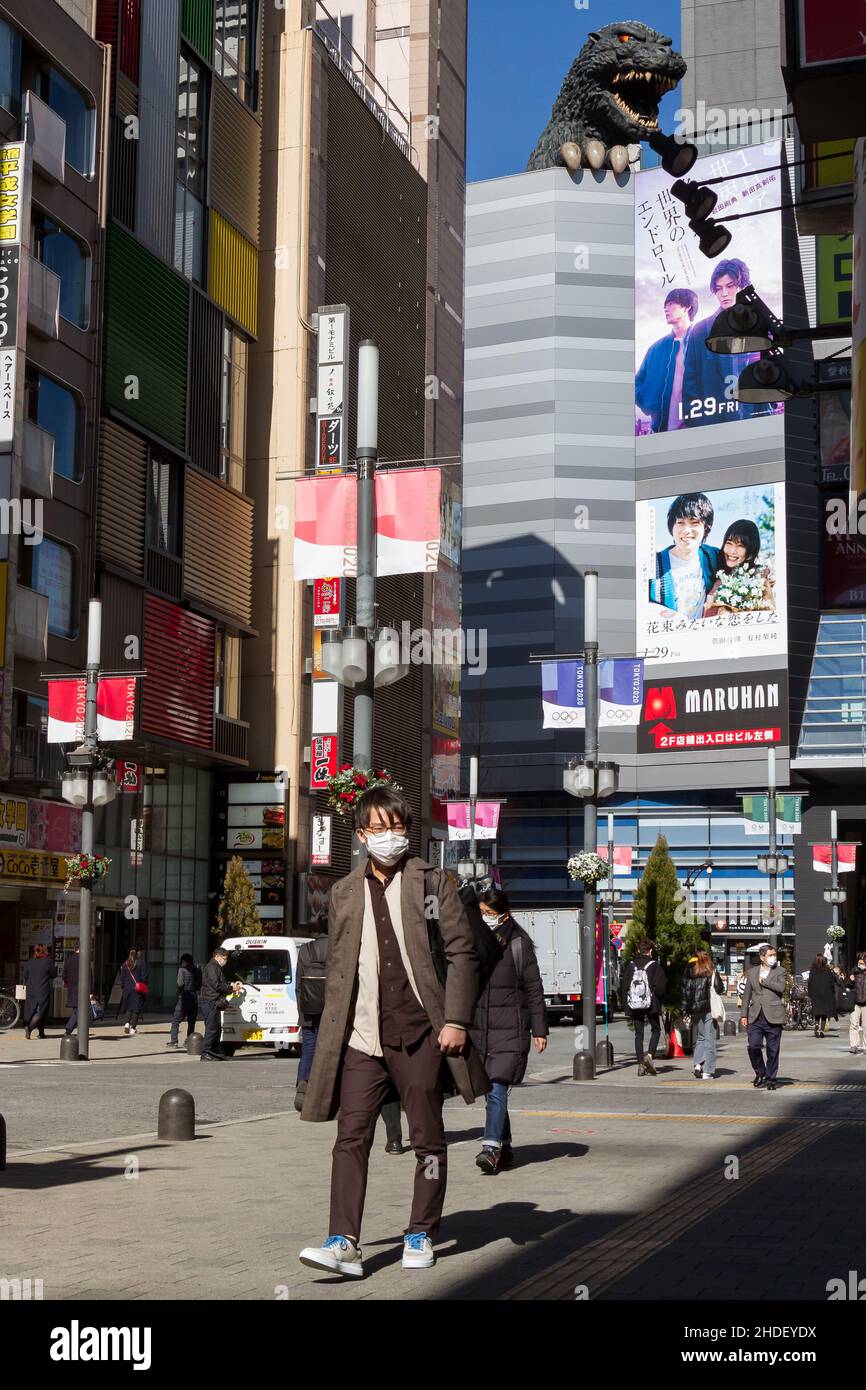 Un uomo giapponese, indossando una maschera chirurgica contro il COVID-19, cammina nel quartiere Kabukicho con un grande modello Godzilla sull'Hotel Gracery alle spalle. Foto Stock