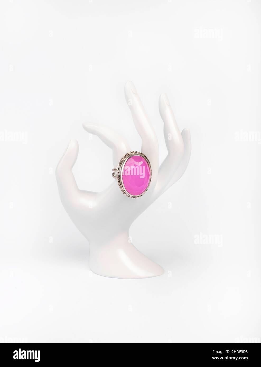 Mano bianca in plastica con anello in argento e quarzo rosa su sfondo bianco Foto Stock
