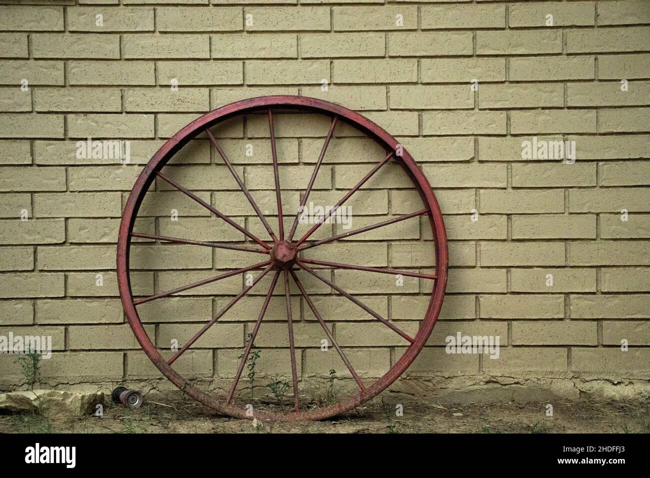 Primo piano di una vecchia ruota rossa del carrello appoggiata su una parete di mattone Foto Stock