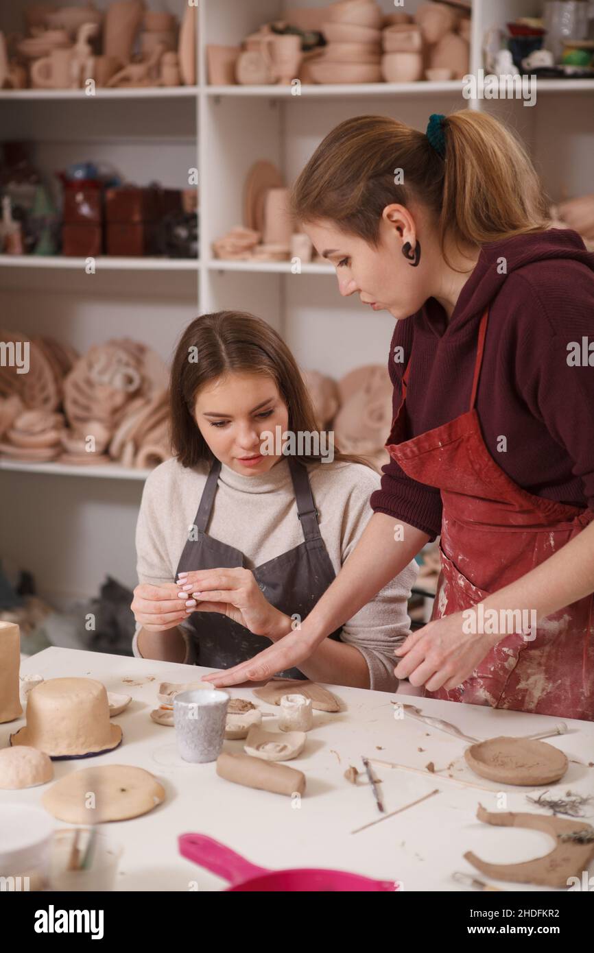 Colpo verticale di una femmina vasaio che insegna giovane donna che lavora con argilla alla classe d'arte Foto Stock