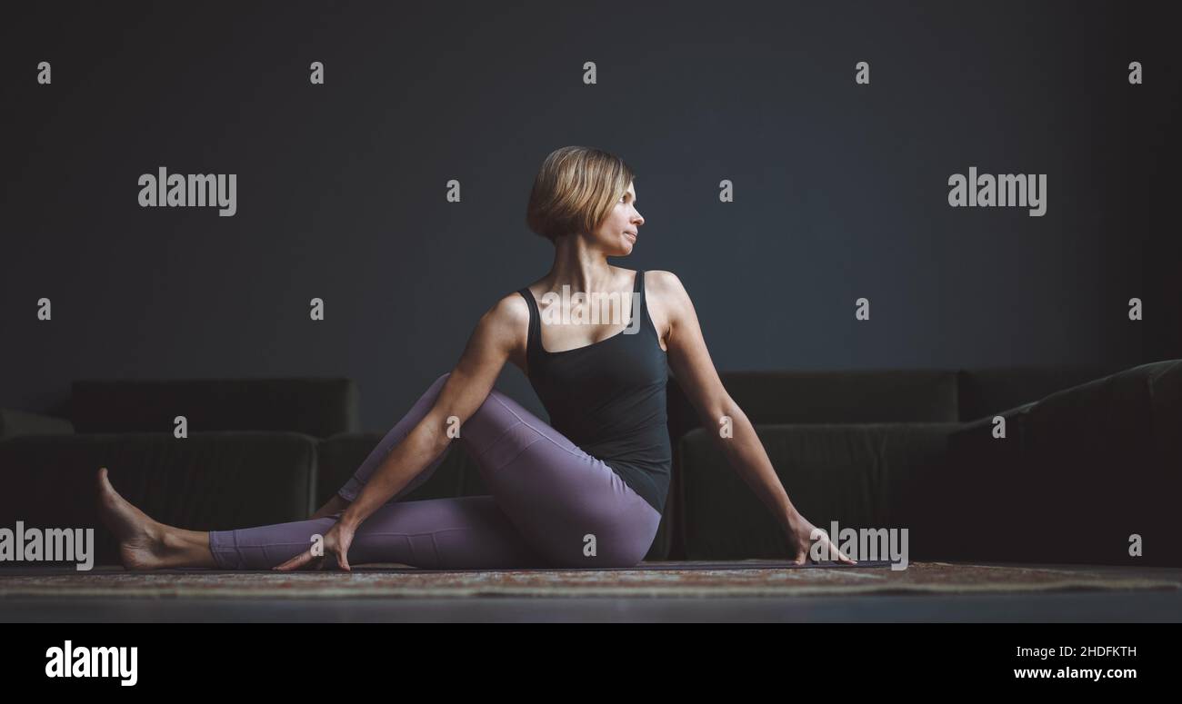 Lezione di yoga. Un corpo bello e addestrato. Una donna fa un asana su uno sfondo scuro in un appartamento di città. Concetto di bellezza del corpo. Foto di alta qualità Foto Stock