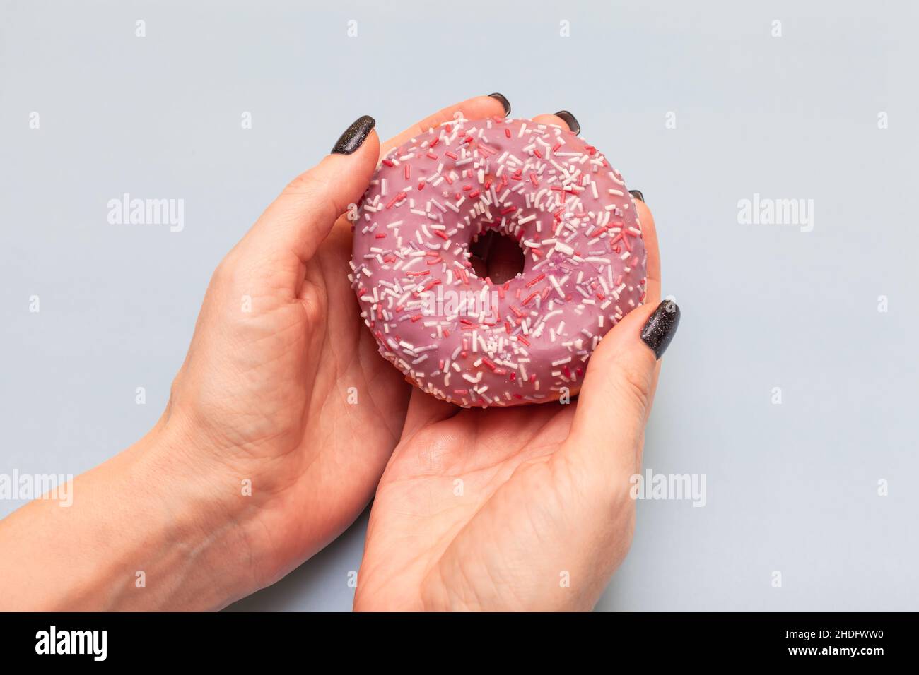 mano femmina che tiene una ciambella luminosa su sfondo azzurro Foto Stock