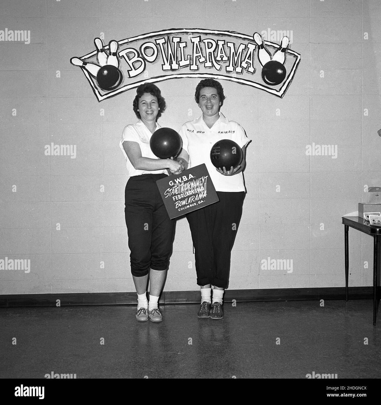1960, storico, due donne adulte dieci-pin bowler nel loro kit di squadra e tenendo le loro palline da bowling, posa per una foto, Columbus, Ohio, USA. Stanno partecipando ad una 'Bowlarama' - segno sul muro dietro di loro - una competizione di bowling tra le squadre. Negli anni 1950s e 60s, oltre ad un popolare passatempo di lessiure negli Stati Uniti, tenpin è stato anche uno sport agonistico amatoriale, con una struttura di campionato organizzata e competitiva, con squadre sia maschili che femminili. La Professional Bowlers Association of America (PBA) è stata fondata nel 1958. Foto Stock