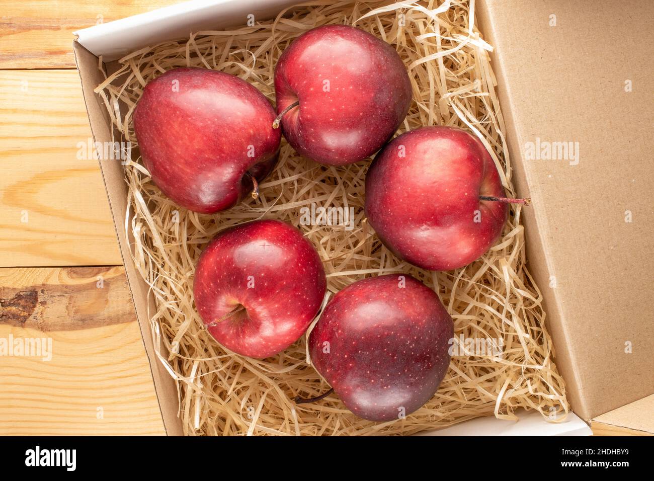 Diverse mele rosse mature in una scatola con trucioli su un tavolo di legno, primo piano, vista dall'alto. Foto Stock