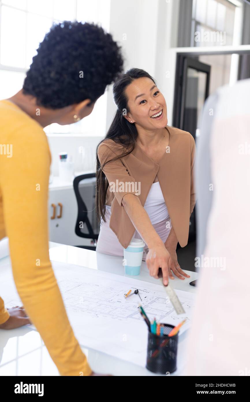 Donna d'affari asiatica sorridente mentre discuteva sopra il blueprint in riunione all'ufficio Foto Stock