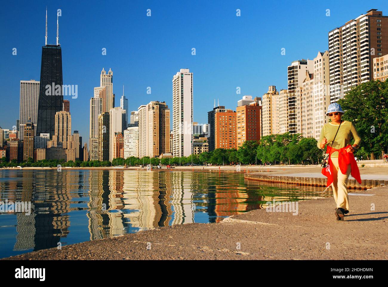 Una donna adulta si esercita camminando lungo il bordo del lago Michigan, in vista del John Hancock Building e dello skyline di Chicago Foto Stock