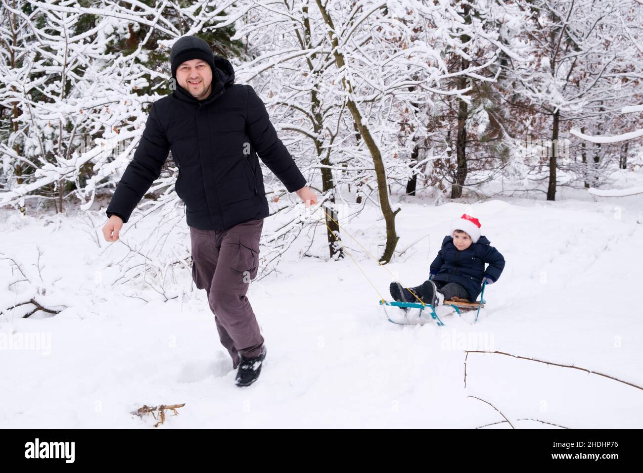 Papà che ha slittato suo figlio in una stazione sciistica in una foresta invernale coperta di neve Foto Stock