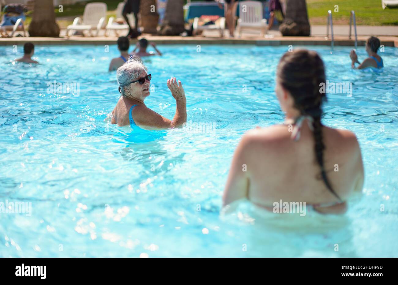 Anziana donna anziana con capelli grigi, con costume da bagno blu che fa aerobica in acqua nella piscina dell'hotel Foto Stock
