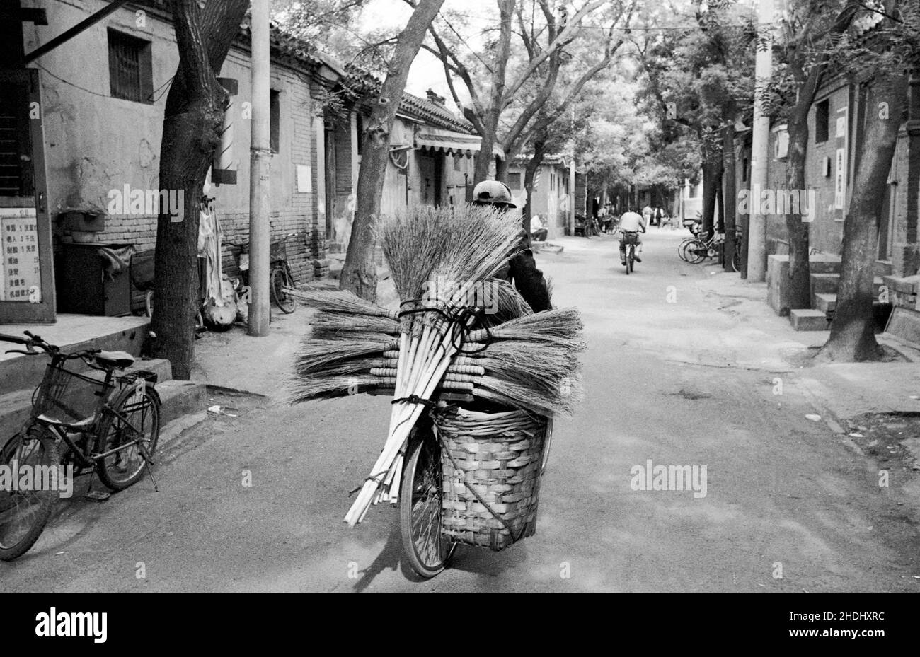 Uomo che porta un carico di spazzole nuove su una bicicletta in un vecchio hutong di Pechino Foto Stock