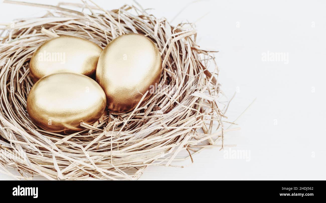 Uova color oro in nido di paglia su tavola bianca, spazio copia Foto Stock
