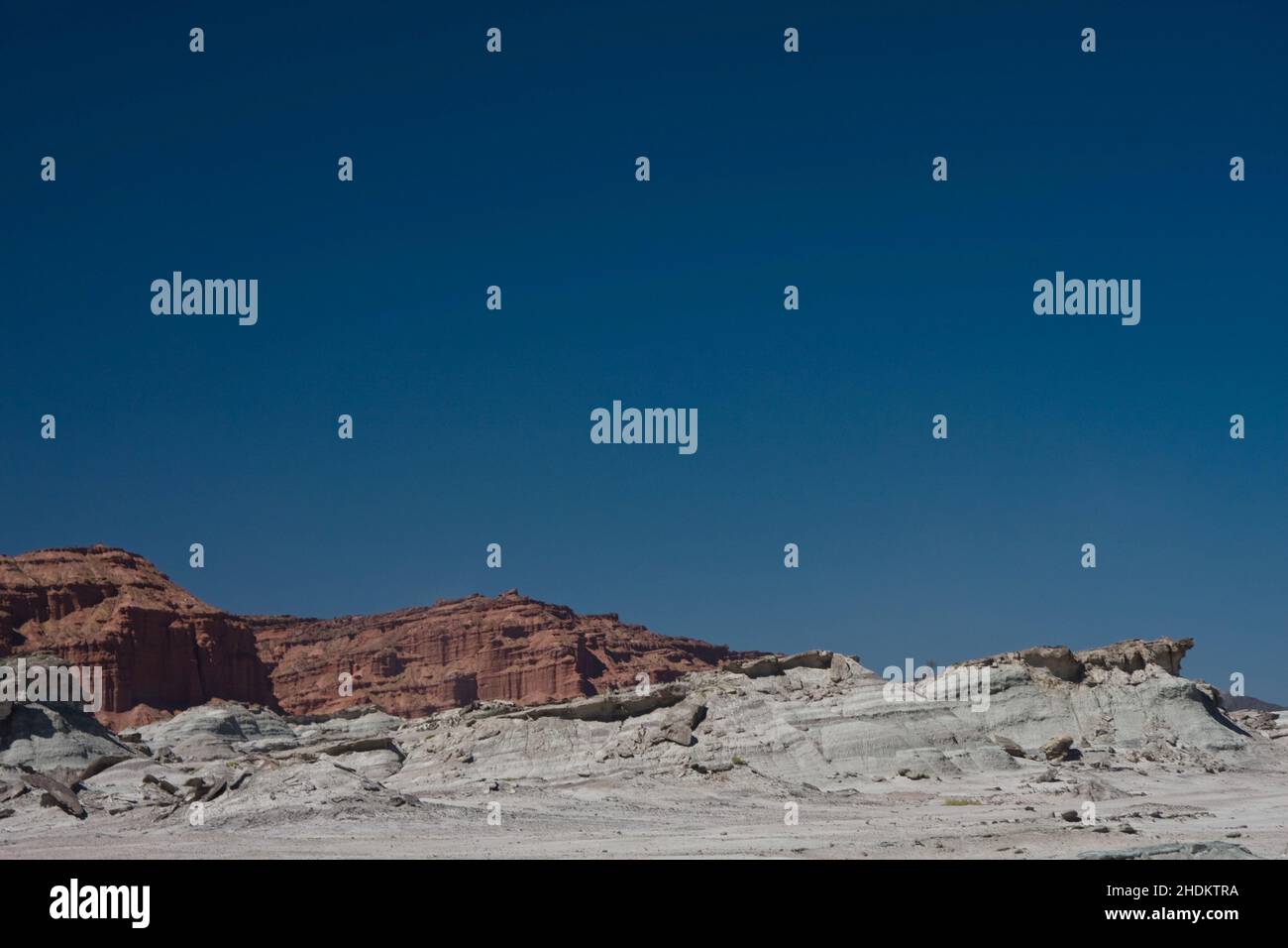 Scatto di un enorme muro di roccia scheggiato in un deserto con lo sfondo di un cielo blu Foto Stock