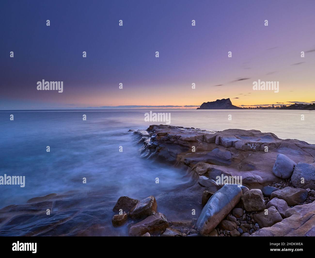 Vista panoramica delle rocce che escono dalla nebbia sotto un cielo color tramonto in una lunga esposizione - carta da parati Foto Stock