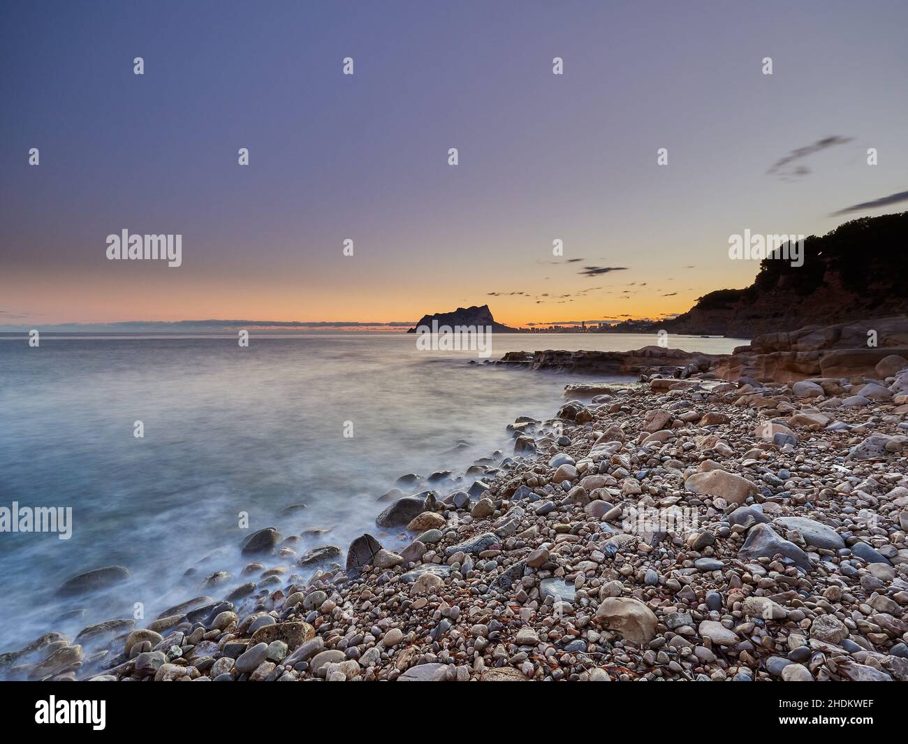 Vista panoramica della costa rocciosa dall'acqua sotto un cielo color tramonto in una lunga esposizione - carta da parati Foto Stock