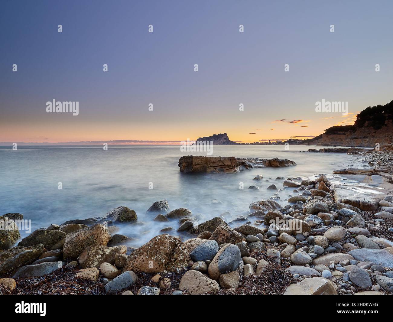 Vista panoramica delle rocce che escono dall'acqua sotto un cielo color tramonto in una lunga esposizione - carta da parati Foto Stock