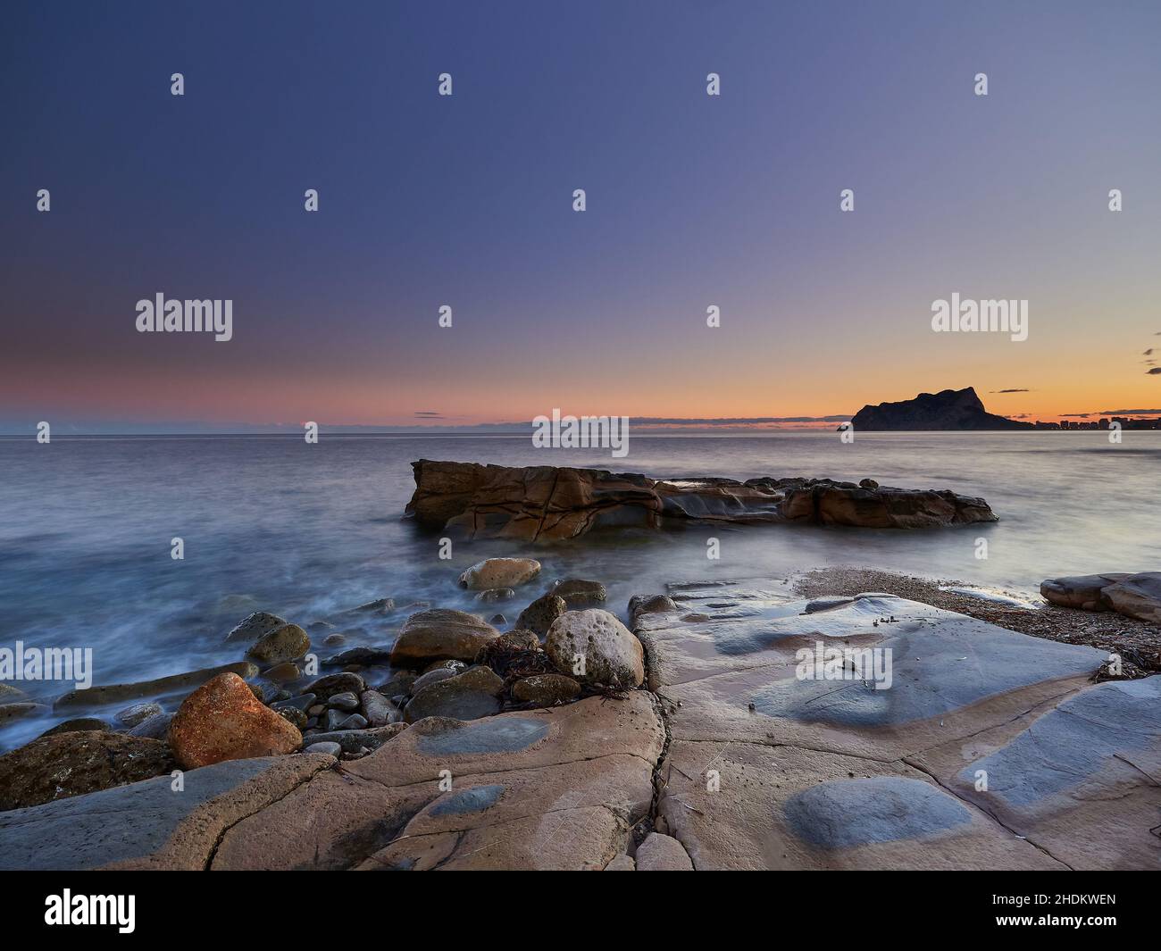Vista panoramica delle rocce che escono dall'acqua sotto un cielo color tramonto in una lunga esposizione - carta da parati Foto Stock