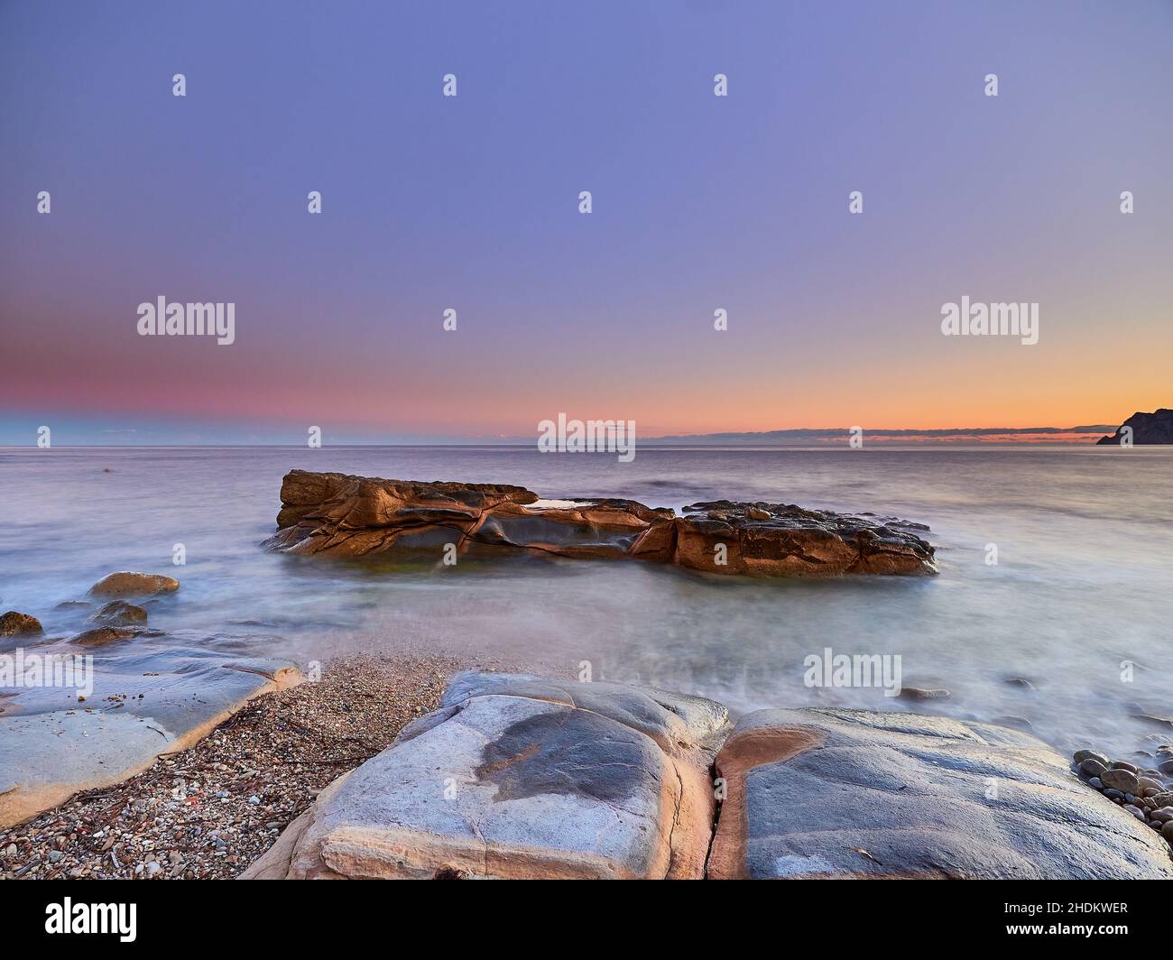 Vista panoramica delle rocce che escono dall'acqua sotto un cielo color tramonto in una lunga esposizione - carta da parati Foto Stock