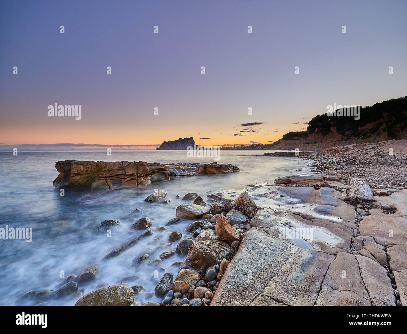 Vista panoramica della costa rocciosa dall'acqua sotto un cielo color tramonto in una lunga esposizione - carta da parati Foto Stock