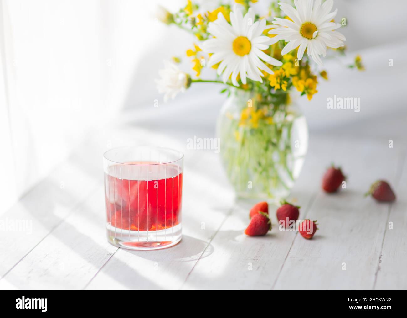 Margherita e fiori gialli in vaso trasparente sul tavolo e bicchiere di bevanda a base di bacche Foto Stock