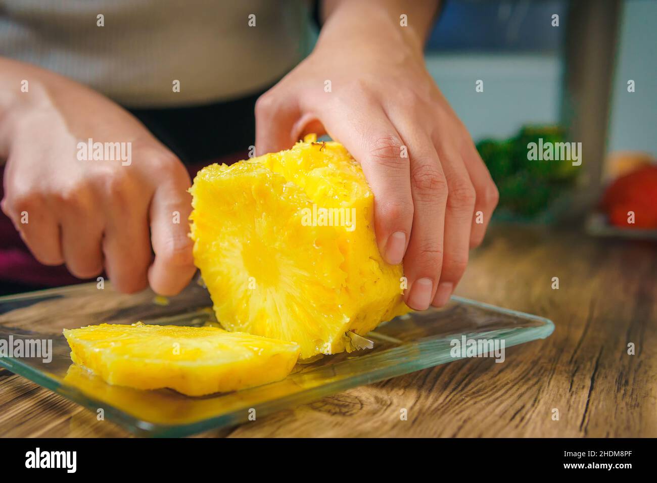 Primo piano delle mani di una giovane donna che taglia un succosa ananas con un coltello dello chef su un tavolo di legno in una cucina. Foto Stock