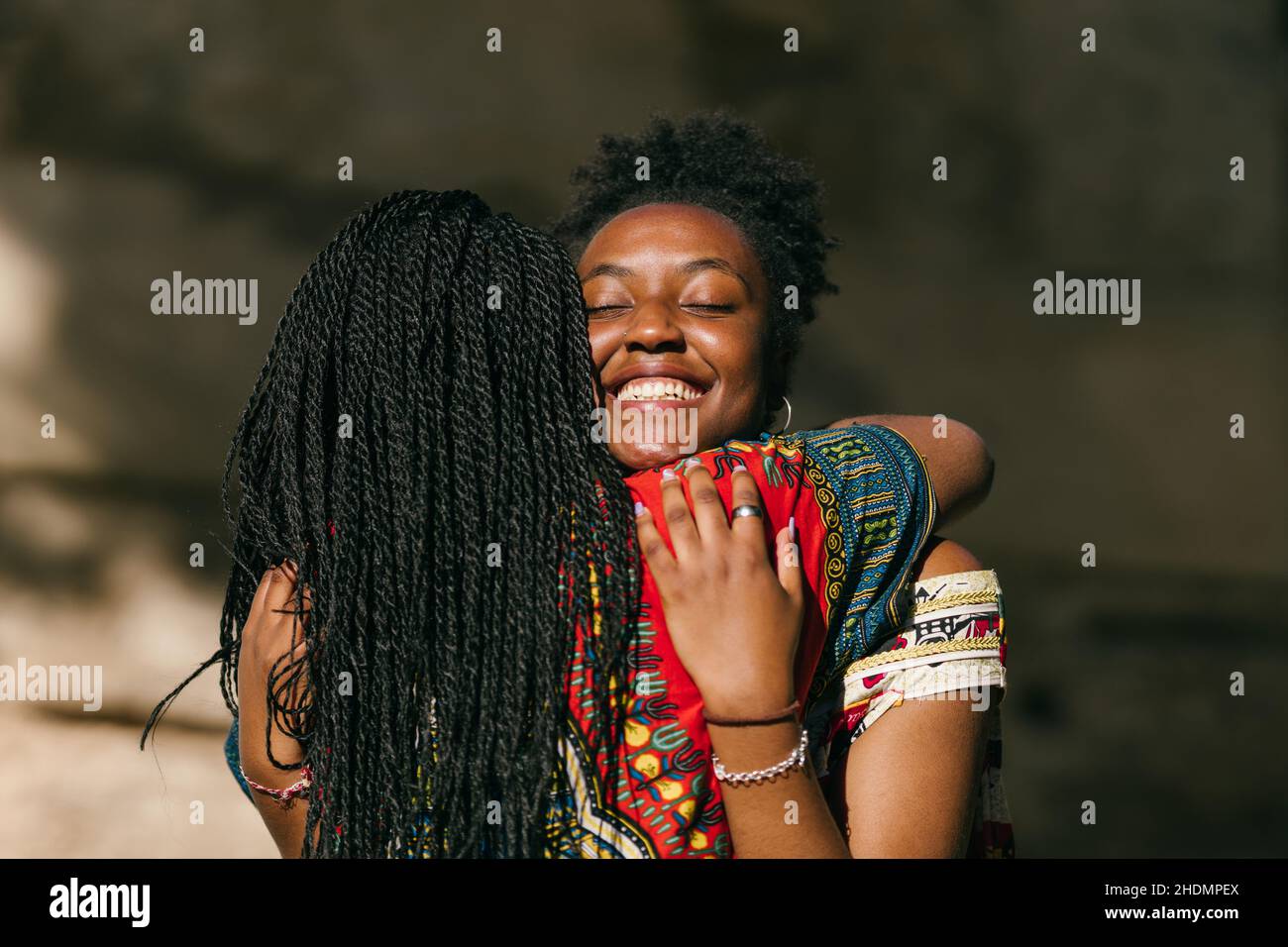 Due donne africane in abiti etnici multicolore che abbracciano emozioni all'aperto Foto Stock