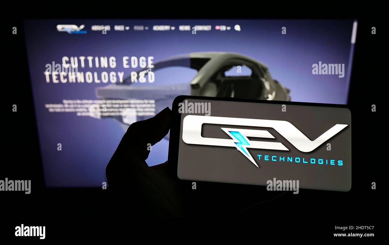 Persona che detiene il telefono cellulare con il logo della società automobilistica spagnola QEV Technologies S.L. sullo schermo di fronte alla pagina web. Mettere a fuoco sul display del telefono. Foto Stock