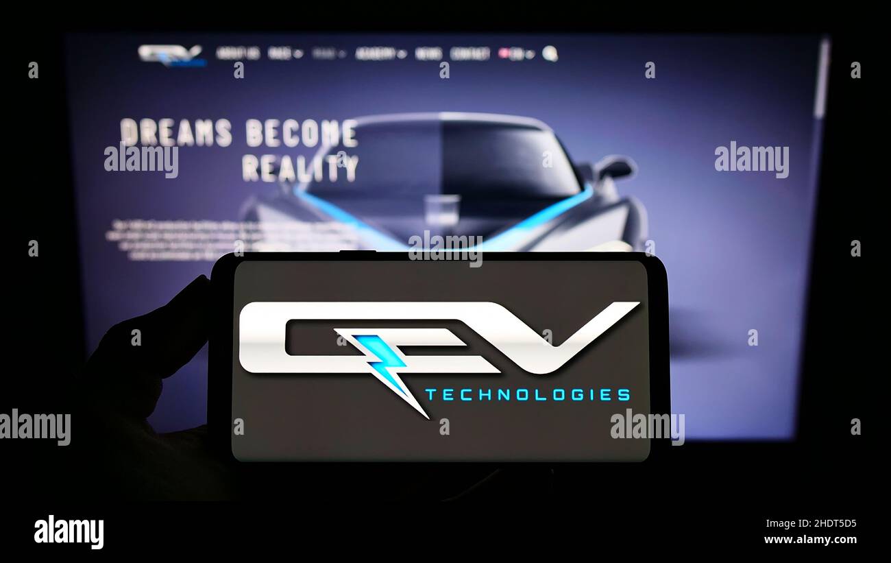 Persona che tiene il cellulare con il logo della società automobilistica spagnola QEV Technologies SL sullo schermo di fronte al sito web. Mettere a fuoco sul display del telefono. Foto Stock