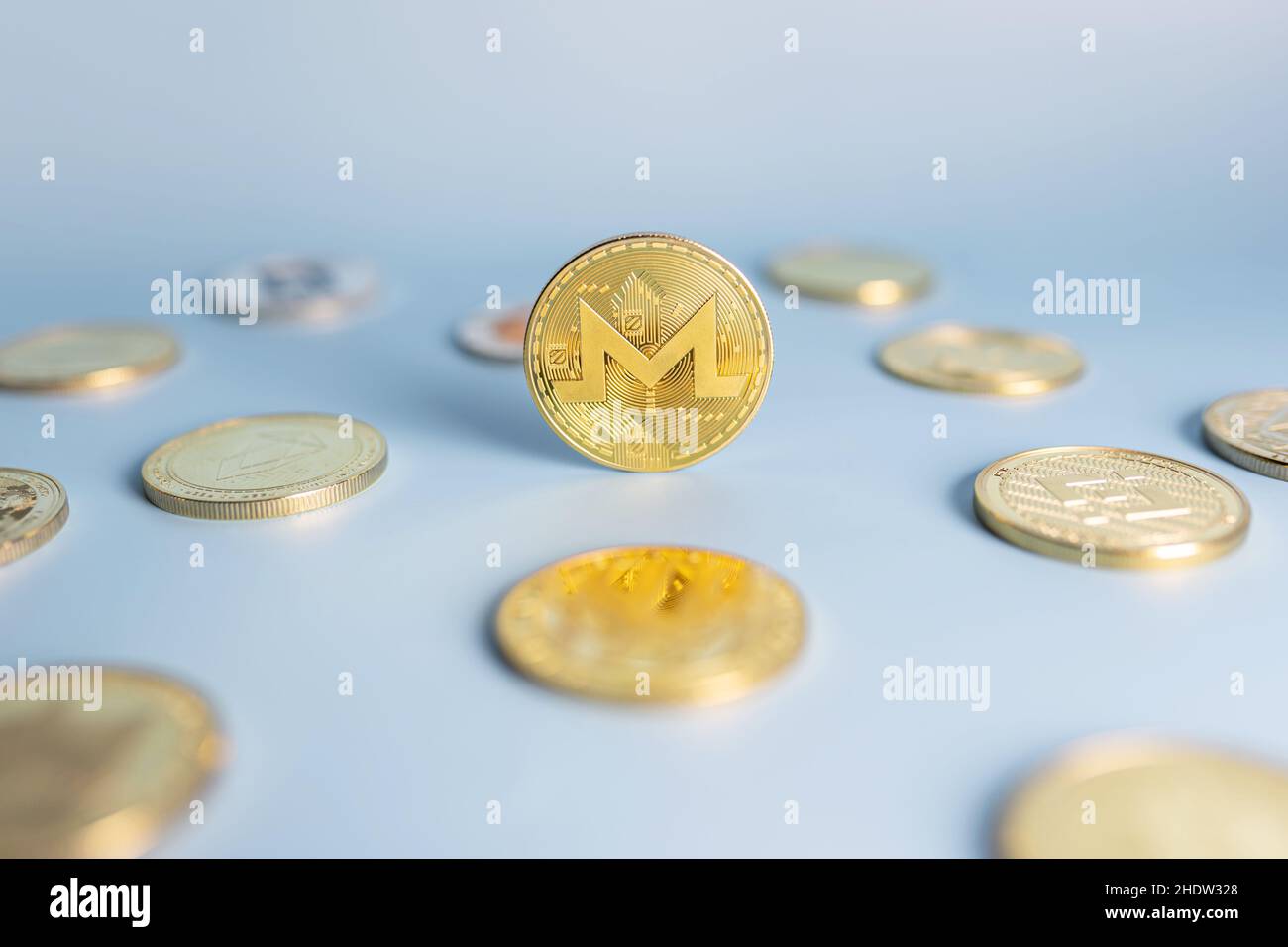 Moneta Monero in piedi in posizione centrale tra un mazzo di monete criptovaluta su sfondo blu. Banner con token criptato XMR dorato. Primo piano, messa a fuoco morbida. Foto Stock