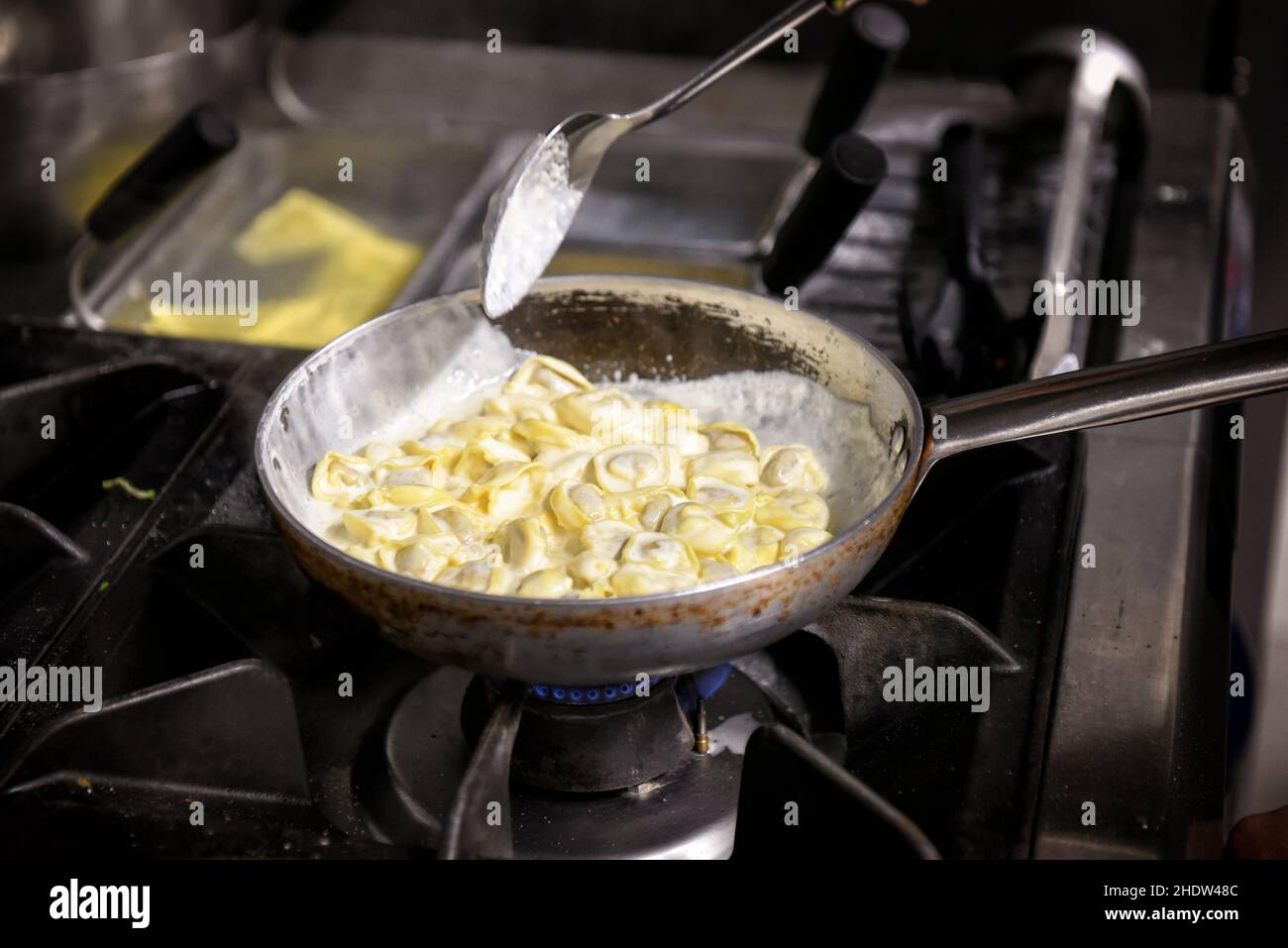 I tradizionali tortellini italiani vengono cotti in padella su un assortimento di ripieno di carne e salsa al formaggio Foto Stock