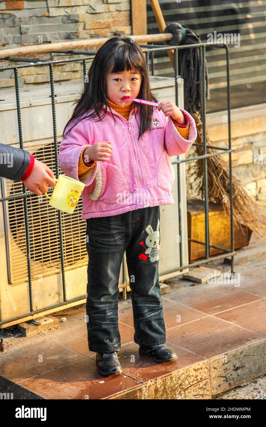 Ragazza che le spazzolava i denti per strada. Tazza d'acqua tenuta da una mano. Jiashan, Cina Foto Stock