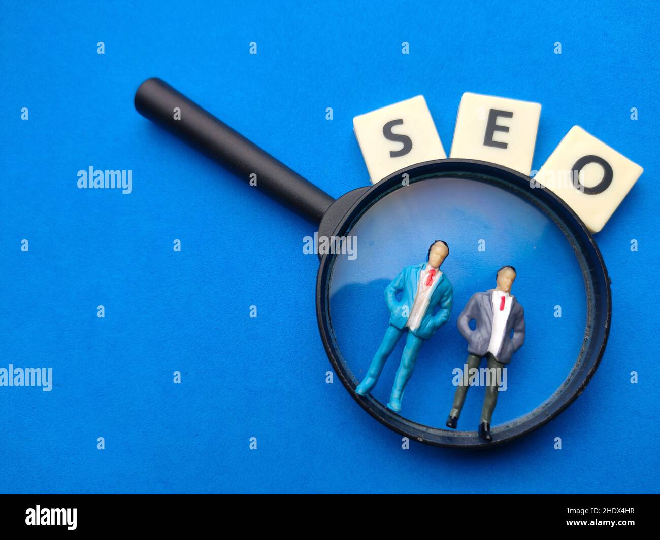 Lente d'ingrandimento, persone in miniatura con parola SEO su sfondo blu. Foto Stock