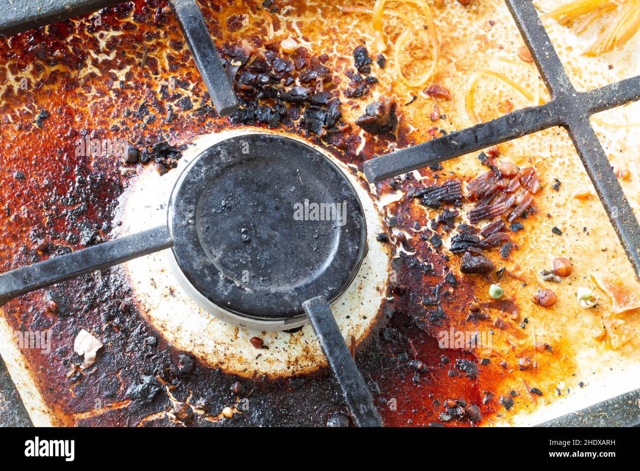 Superficie di stufa a gas sporca. Bruciatore a gas e griglia in ghisa di un forno a gas circondato da vecchi avanzi di cibo e bevande. Superficie area superiore e bruciatore Foto Stock