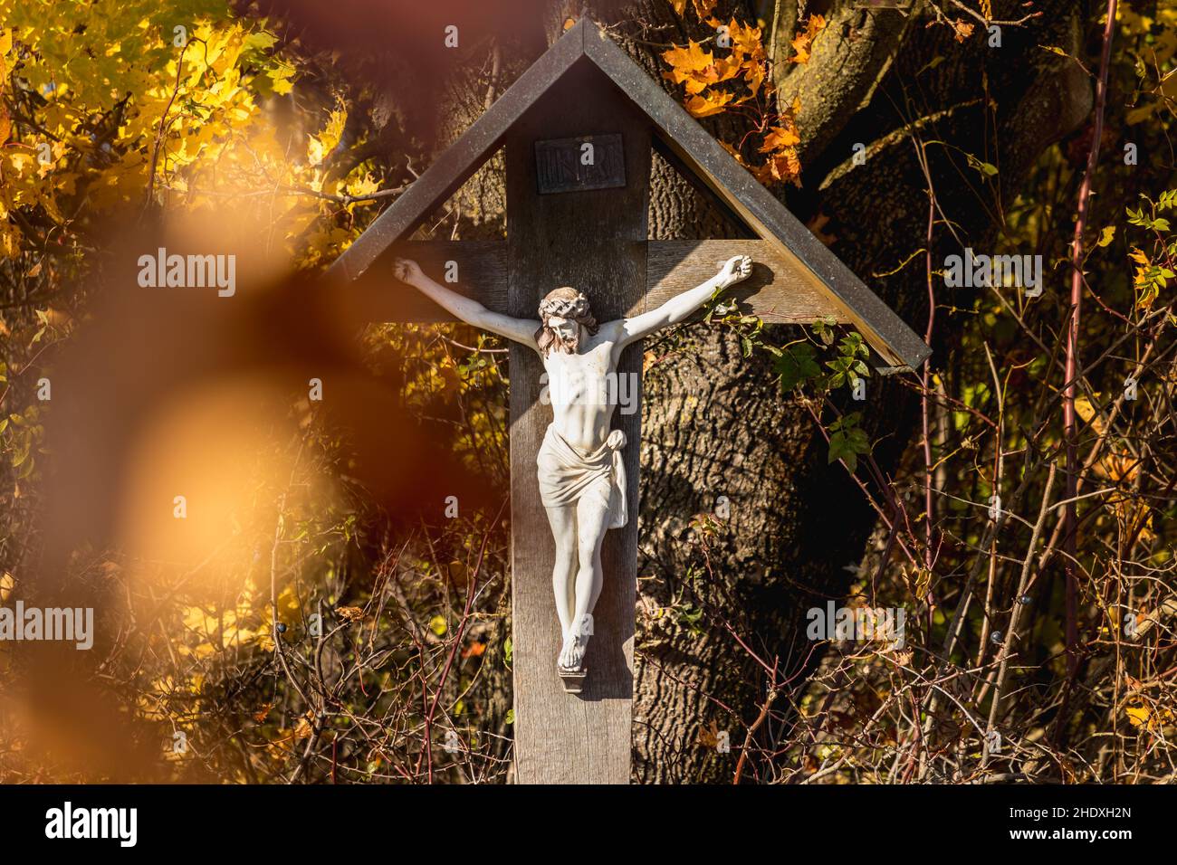 Una croce lungo la strada in Baviera, foglie d'autunno marroni incorniciano Gesù Foto Stock