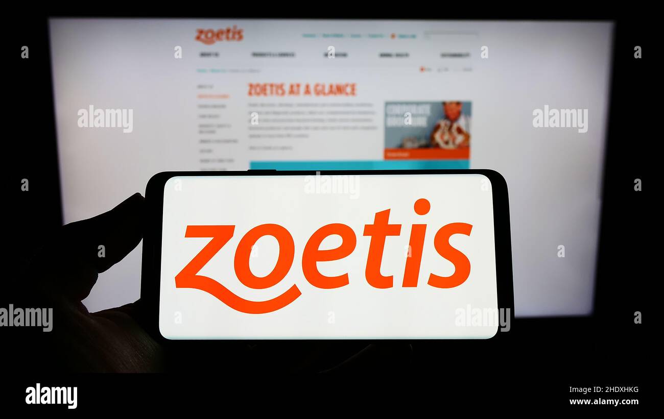 Persona che tiene smartphone con il logo della compagnia statunitense Zoetis Inc. Di droga animale sullo schermo di fronte al sito web. Mettere a fuoco sul display del telefono. Foto Stock
