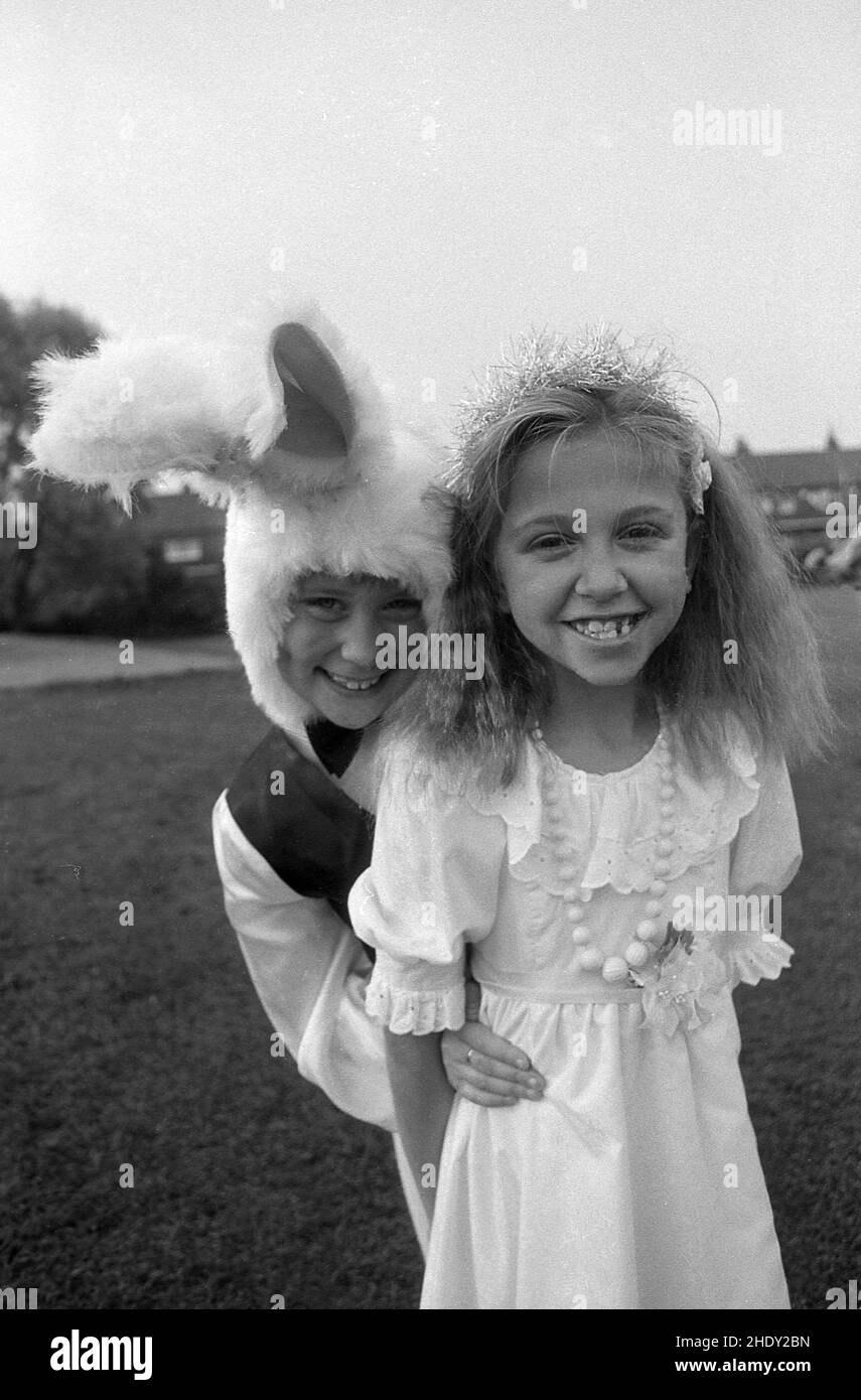 1980s, storico, pasqua e due bambini piccoli vestiti, uno con un berretto di furry, Inghilterra, Regno Unito. Pasqua è un momento divertente per i bambini, con la donazione e la ricezione di uova di pasqua. Un coniglio immaginario, il coniglietto pasquale si crede di portare doni al rene in questo momento. Come conigli danno tradizionalmente alla luce molti bambini, il coniglietto pasquale è anche un simbolo di vita nuova. La tradizione risale ai tempi pagani. Foto Stock