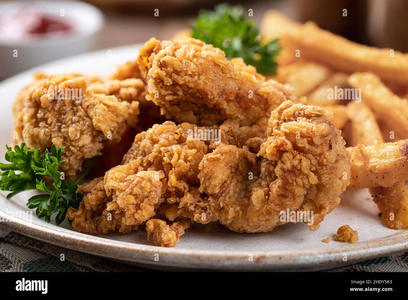 Primo piano di pollo fritto croccante e patatine fritte guarnite con prezzemolo su un piatto Foto Stock