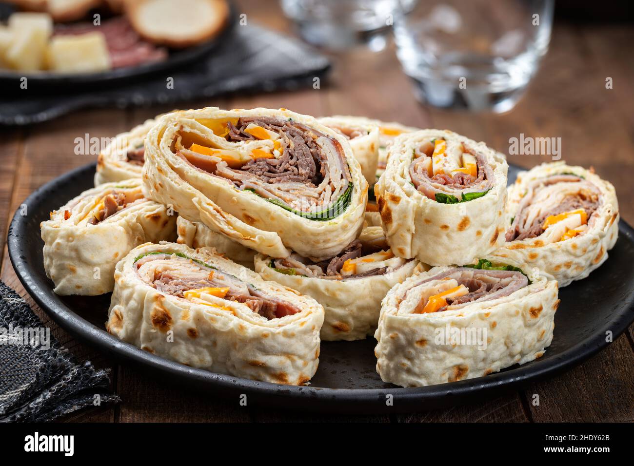 Tortilla involtini fatti con roast beef, tacchino, formaggio e lattuga su un piatto nero Foto Stock