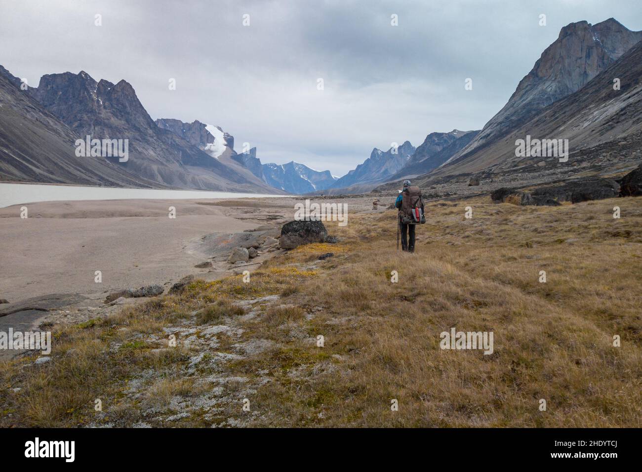 Escursionista con uno zaino pesante che cammina in una remota valle artica in una giornata nuvolosa. Spettacolare paesaggio artico del Passo di Akshayuk, Isola di Baffin, Canada. Mt Foto Stock