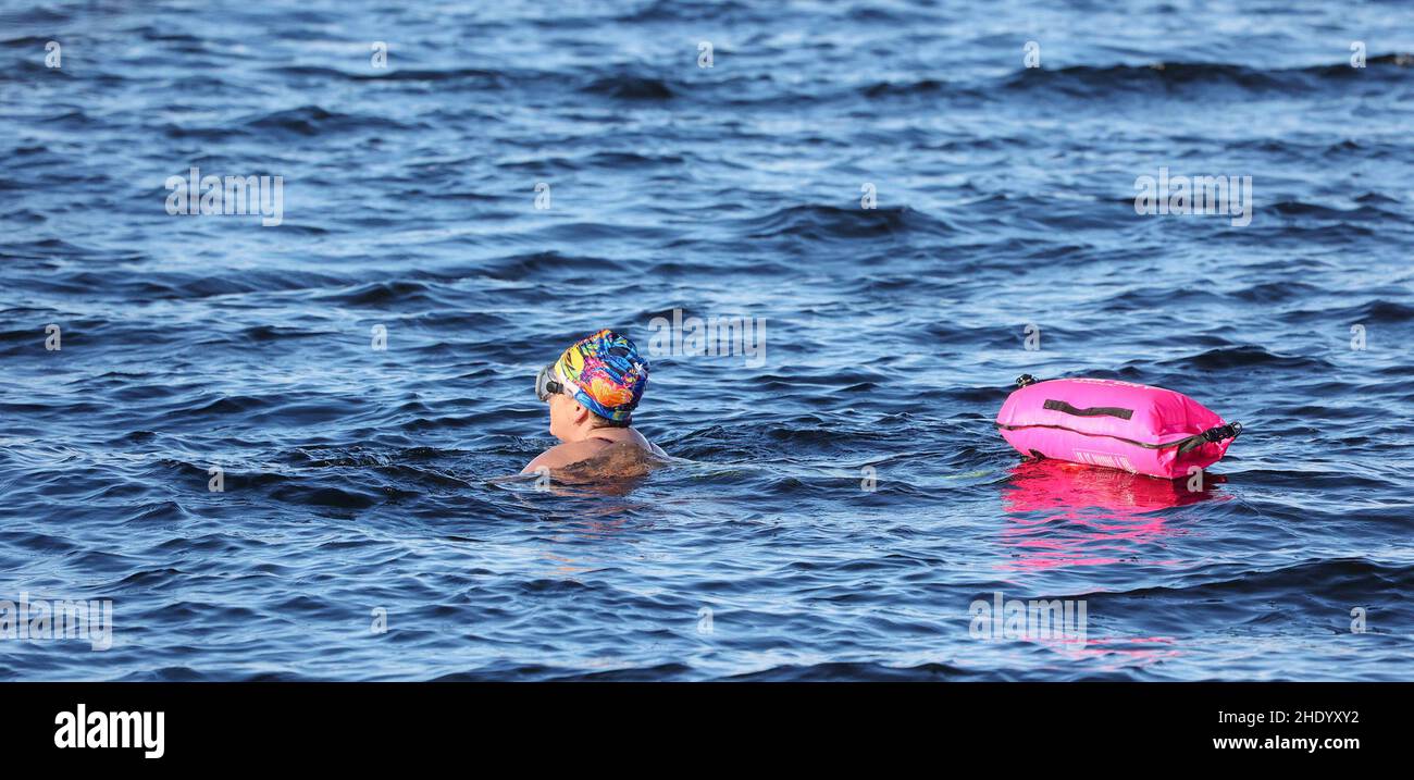 Oxford Island, Lough Neagh, Irlanda del Nord. 07 Jan 2022. Tempo britannico - una giornata luminosa con la doccia occasionale del wintry dopo la notte neve nell'Irlanda del Nord. Nuotatore femminile in acqua aperta con galleggiante rosa che gode degli effetti rinvigorenti del nuoto invernale. La temperatura dell'acqua era di 3,3C che sarebbe stata leggermente più calda della temperatura dell'aria all'epoca. Credit: CAZIMB/Alamy Live News. Foto Stock