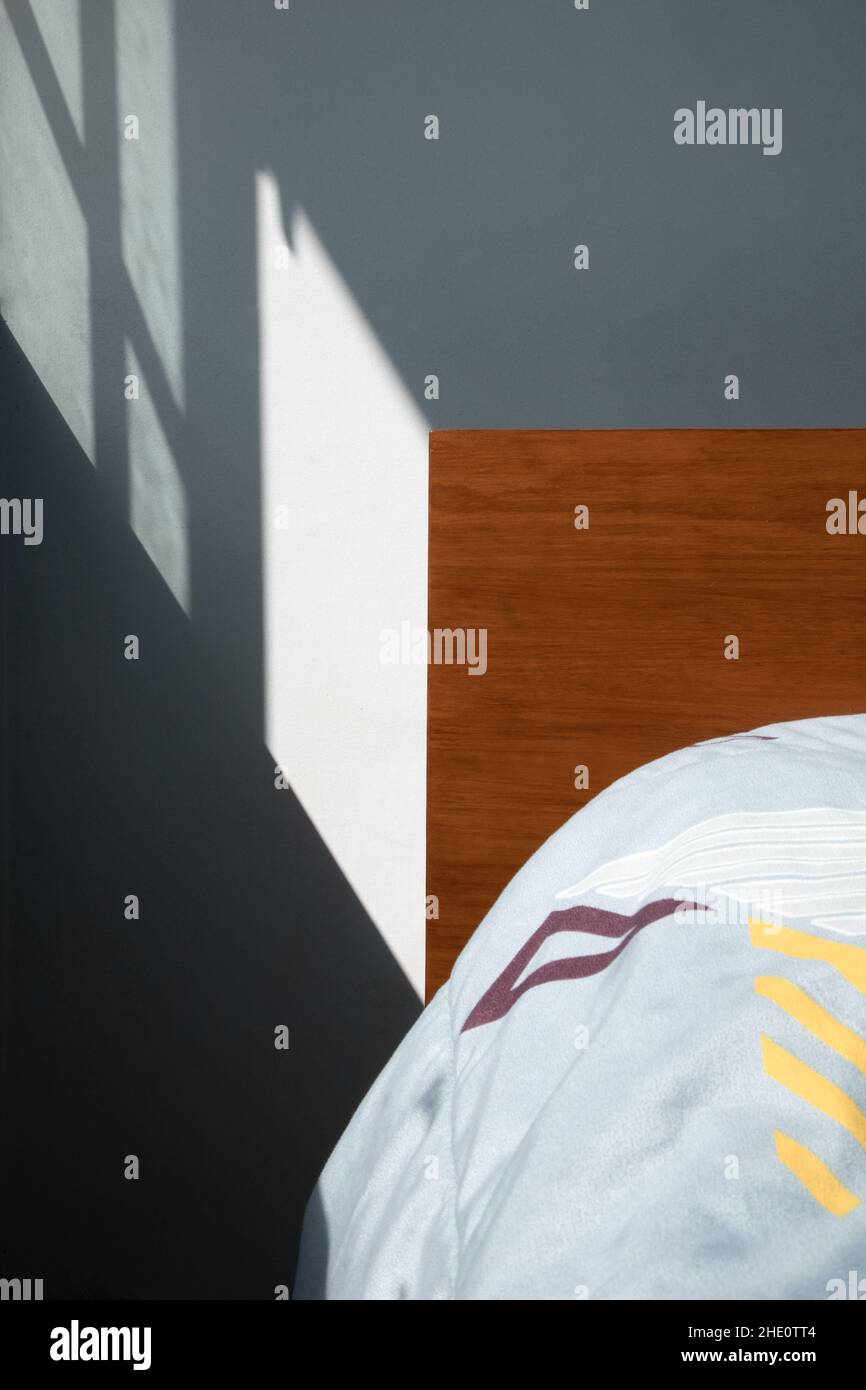 dettagli dell'angolo di una testiera in legno di un letto con una trapunta blu chiaro con figure geometriche, mobili e decorazioni in una giornata di sole con capannone Foto Stock