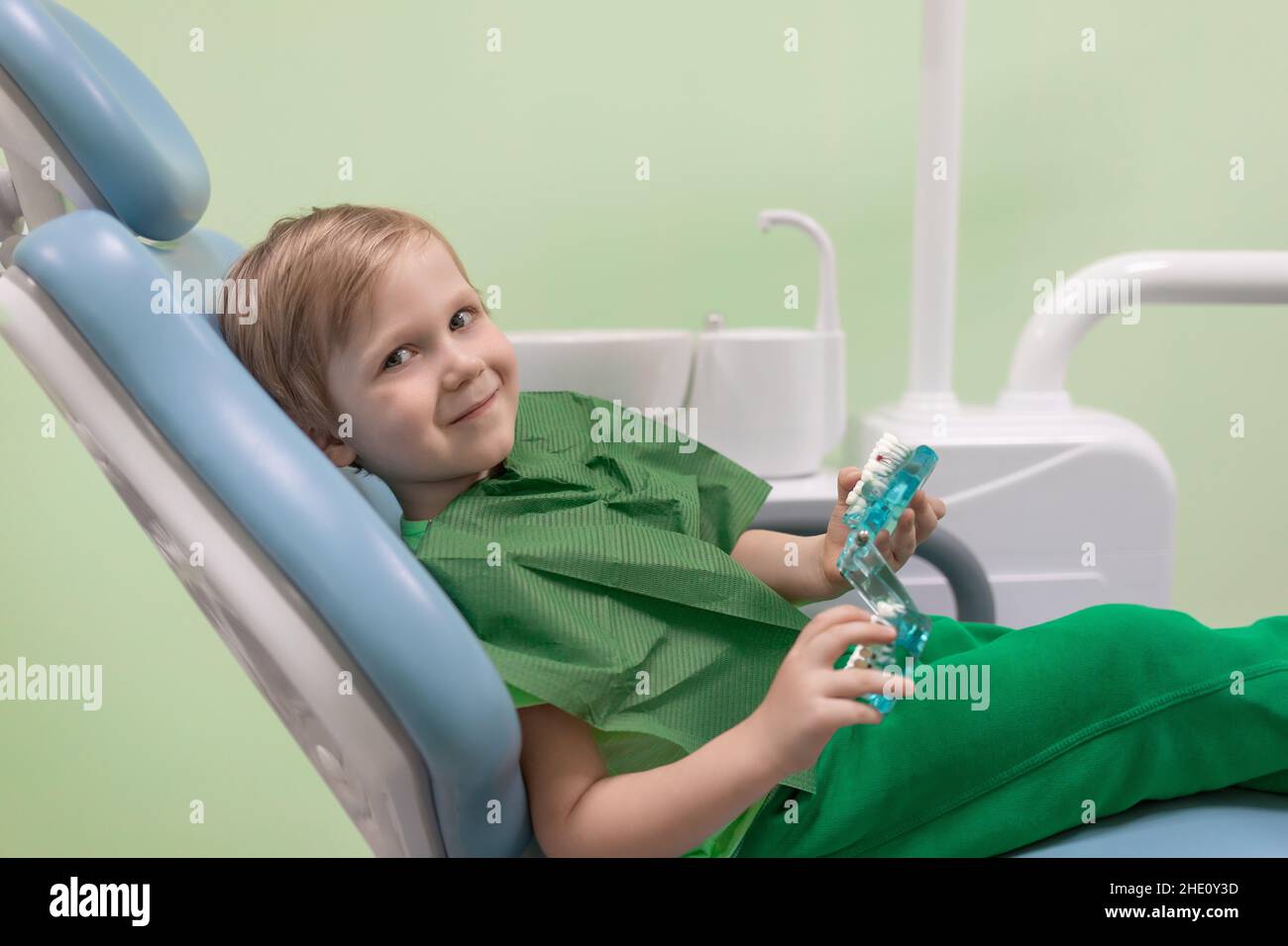 Il bambino caucasico esamina i denti trattare nella mandibola sulla sedia al dentista, primo piano. Concetto per odontoiatria pediatrica, giochi e giocattoli in clinica. Vista laterale. Foto Stock