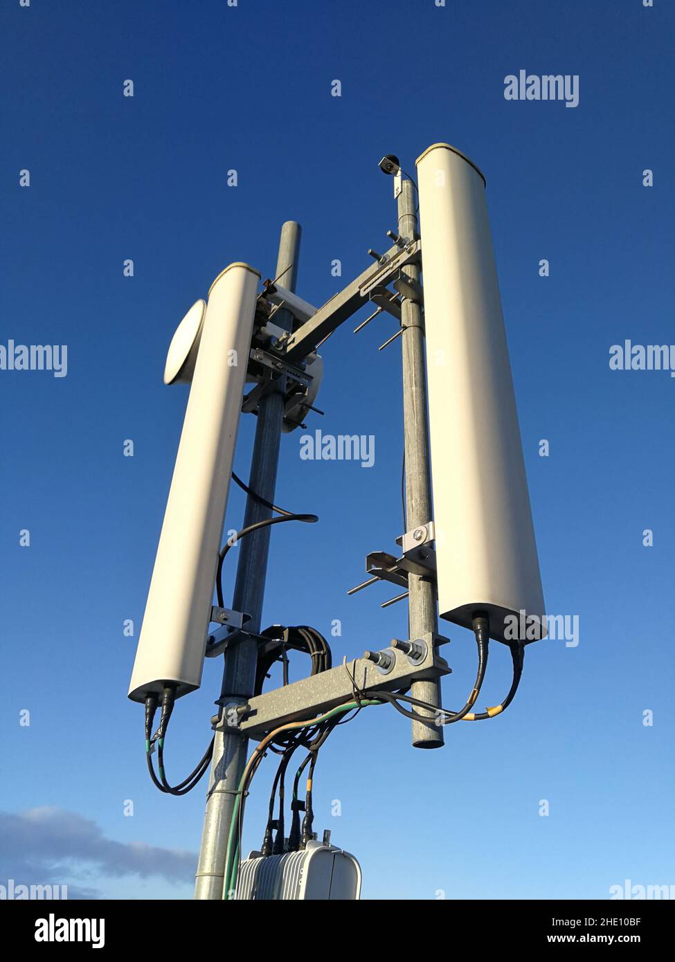 Stazione base GSM (Global System for Mobile Communication) e ripetitore di fronte al cielo blu nuvoloso per le telecomunicazioni Foto Stock