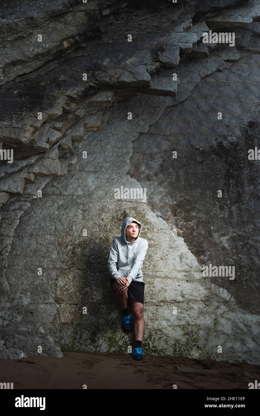 Pensieroso adolescente ispanico attivo contro la parete della scogliera Foto Stock
