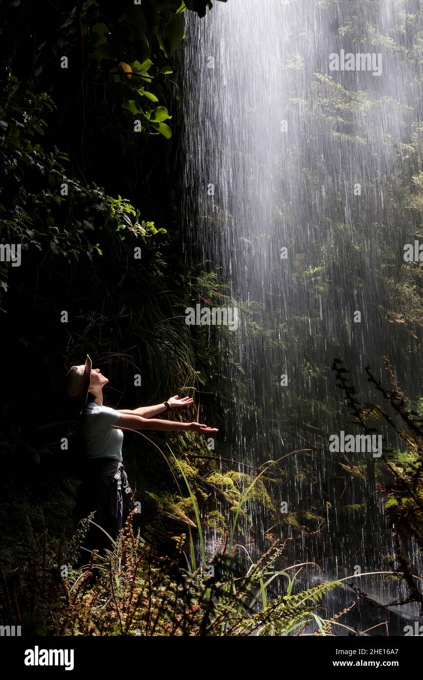 donna escursionista in un cappello che estende le mani sotto la cascata fredda spray Foto Stock