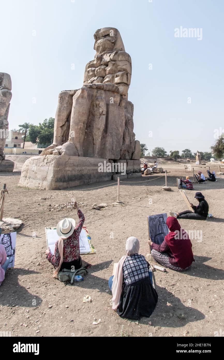 Presso il sito storico dei Colossi di Memnon, un gruppo di studenti d'arte egiziani si siedono e disegnano le antiche statue nei loro pattini. Foto Stock