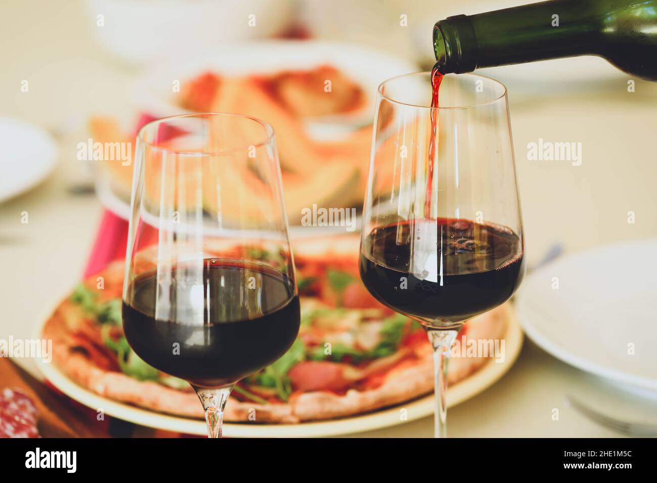 Versare il vino rosso dalla bottiglia in bicchieri sul tavolo con fondo alimentare Foto Stock