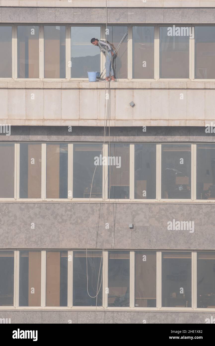 Una lavafinestre al Cairo, Egitto lavora per pulire il vetro di un alto edificio molti piani in su. Lavori pericolosi con attrezzatura di sicurezza minima. Foto Stock