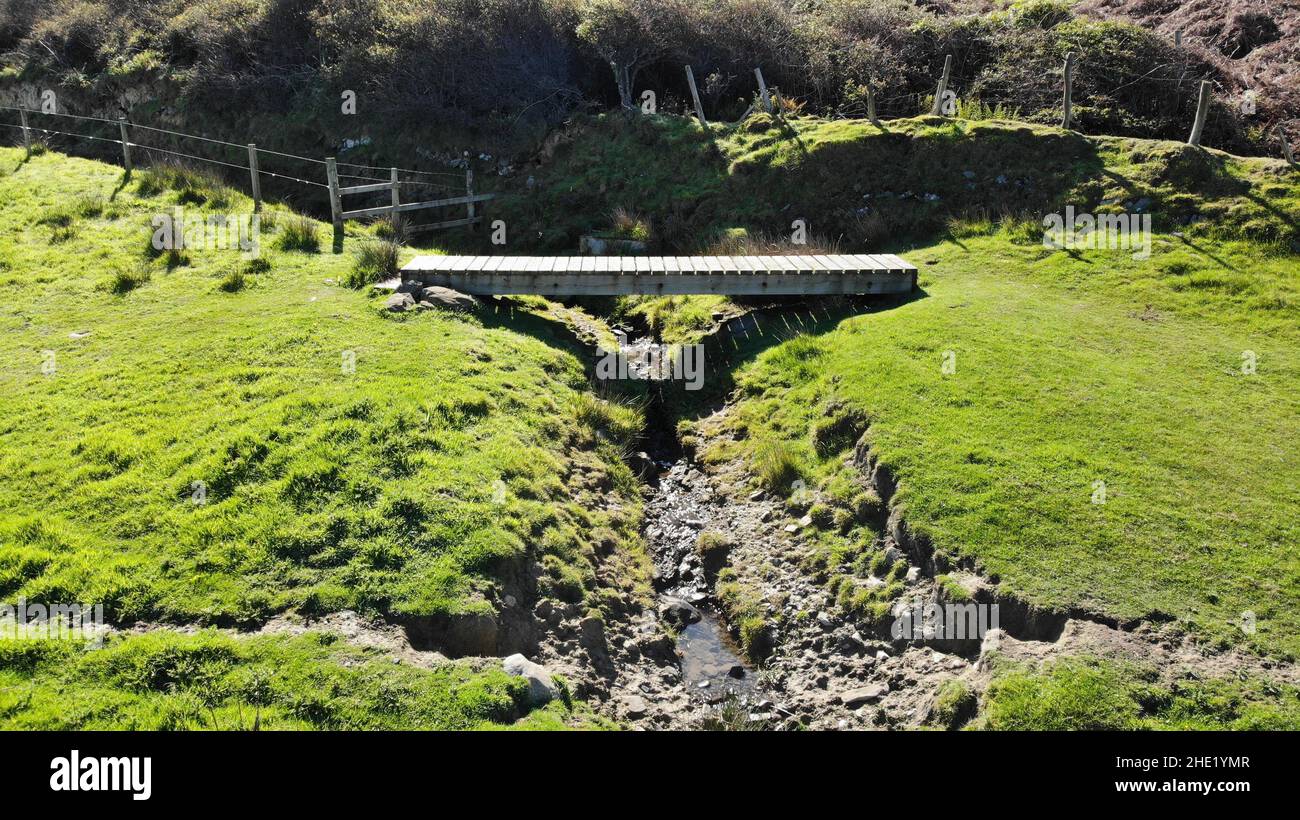 Immagine aerea di un ponte di legno lungo il Llanon, sentiero costiero Ceredigion. Mostra cespugli di gorse sullo sfondo e un ruscello Foto Stock