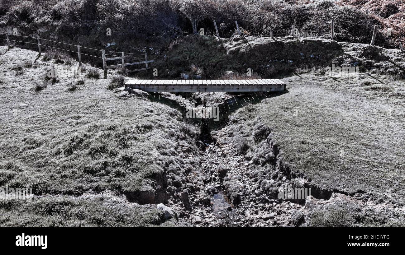 Immagine aerea di un ponte di legno lungo il Llanon, sentiero costiero Ceredigion. Mostra cespugli di gorse sullo sfondo e un ruscello Foto Stock