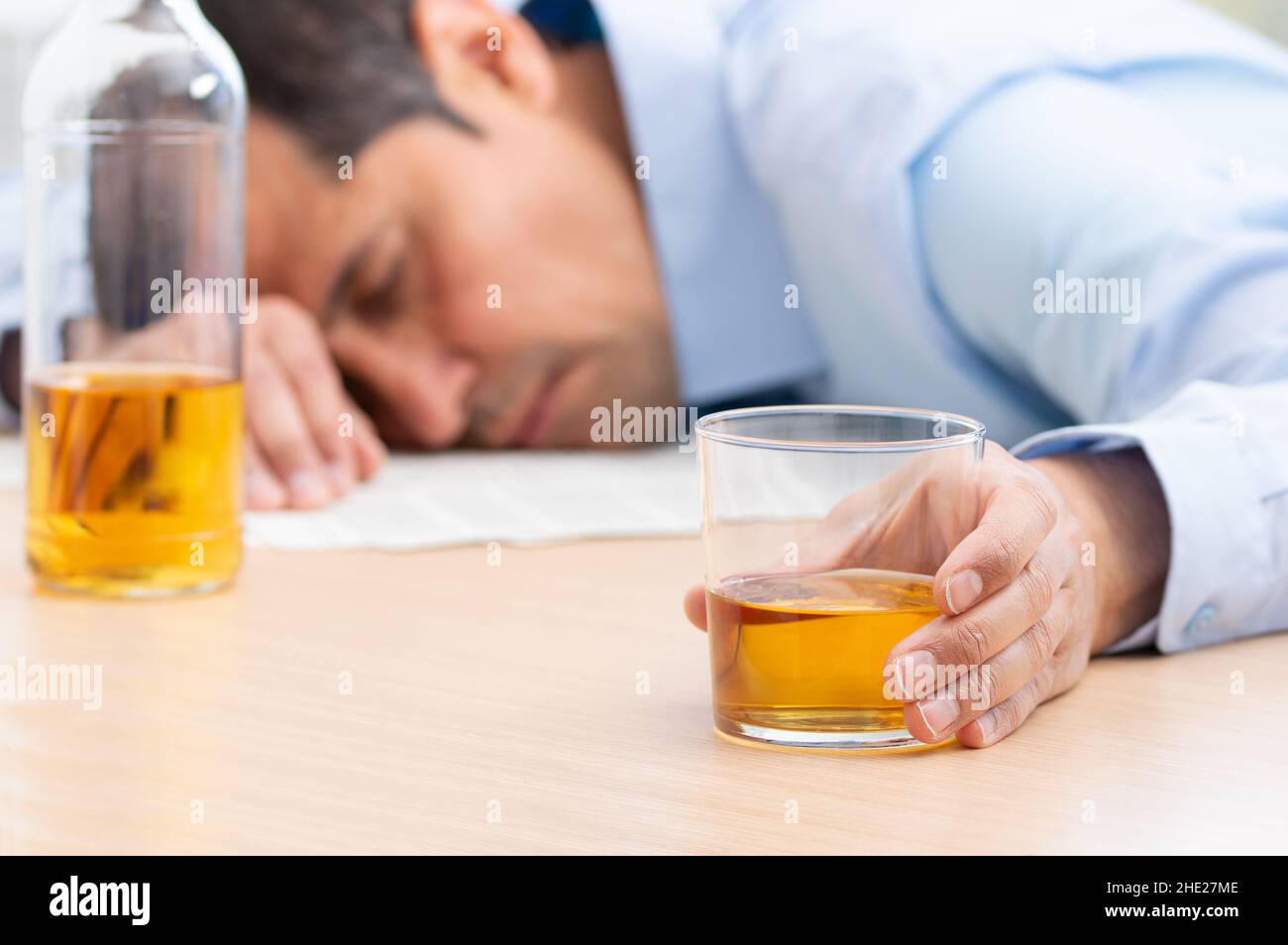 Primo piano di un uomo d'affari stressato che tiene un bicchiere di whiskey che dorme e Data Charts, documento di affari alla scrivania dell'ufficio. Dipendenza da alcol e ubriaco Foto Stock