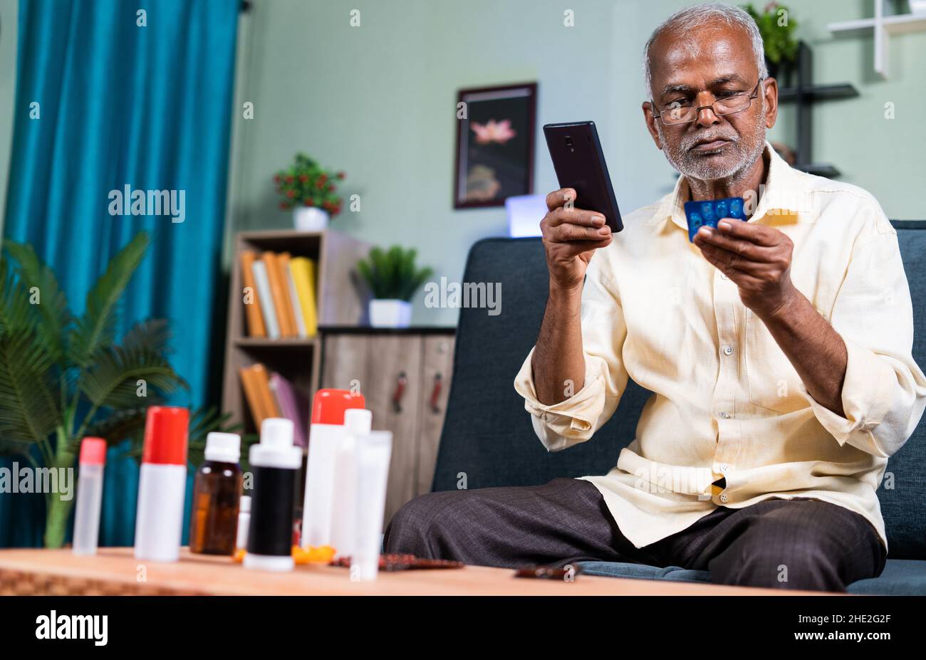 Uomo anziano che controlla la disponibilità, l'acquisto o l'ordinazione di medicinali online sul telefono cellulare da casa - concetto di e-Pharmacy Foto Stock